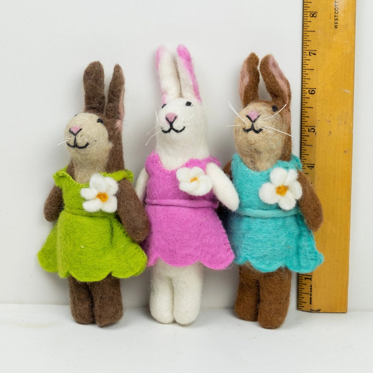 
                  
                    fair trade felt bunnies in green, pink, and teal outfits, by a ruler the winding road
                  
                