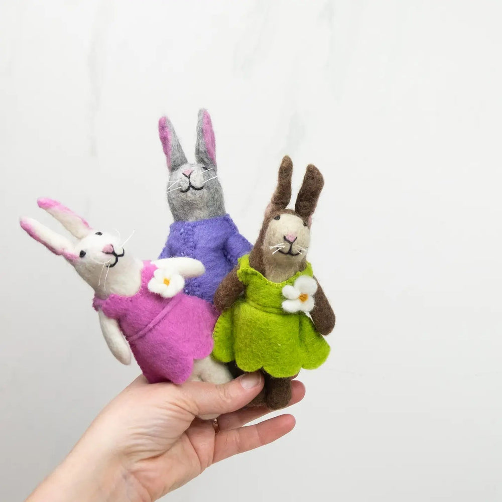 
                  
                    fair trade felt bunnies in pink, purple,a nd green outfits held in hand by the winding road
                  
                